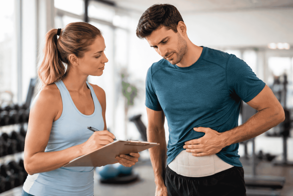 Man with hernia support belt talking to trainer in gym