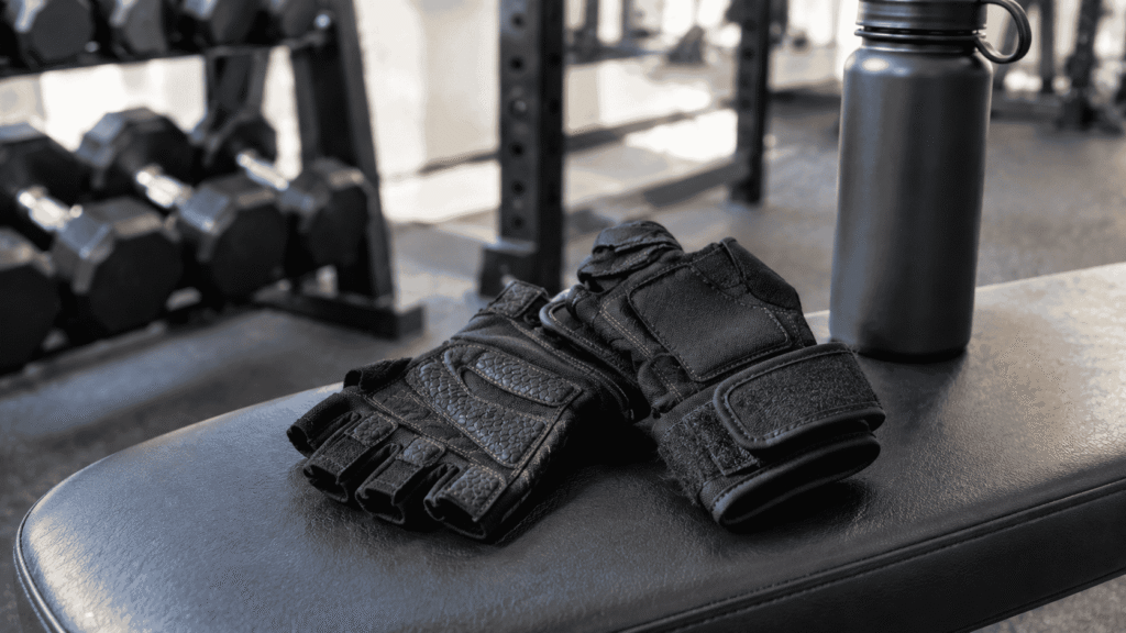 Pair of black weightlifting gloves on a gym bench with dumbbells in the background